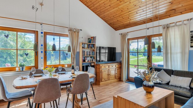 A spacious living area with a wooden ceiling, large windows, a dining table, and a sofa. - Ferienhaus Bude 87 by Interhome (Bad Arolsen)