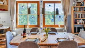 A dining room with a large wooden table set for four, a wine bottle, and a vase with flowers. - Ferienhaus Bude 87 by Interhome (Bad Arolsen)