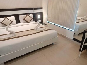 A hotel room with a large bed, a nightstand, a mirror, and a window with a view. - Yuvraj Palace Inn (Mysore)