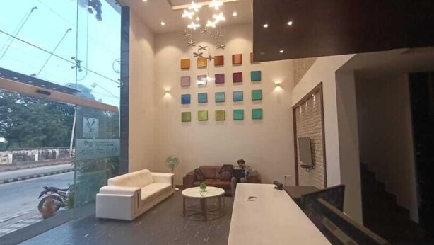 A modern lobby with a large window, a sofa, a coffee table, and a wall with colorful square decorations. - Yuvraj Palace Inn (Mysore)