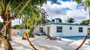 Ein Strandhaus mit Pool, Palmen und einer Hängematte.
