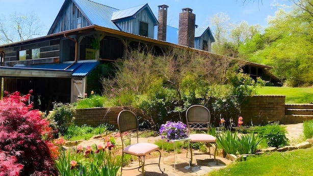 A large house with a blue roof and stone chimneys, surrounded by a garden with chairs and flowers. - Secluded Estate Sleeps 8 with 1 acre fishing pond  (Mount Pleasant)