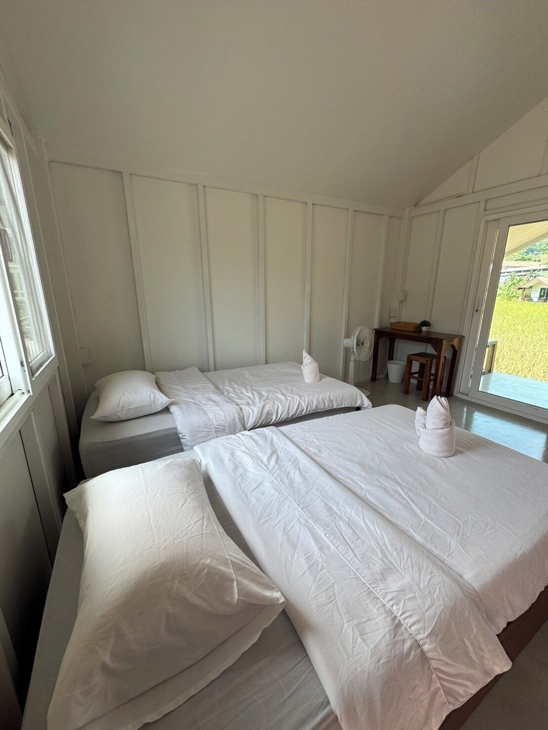 A room with two beds, a small table, and a window with a view of greenery.