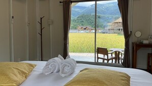 A hotel room with a bed, two towels, a view of a rice field, and a table with chairs. - Sapan Dee View (Bo Kluea)