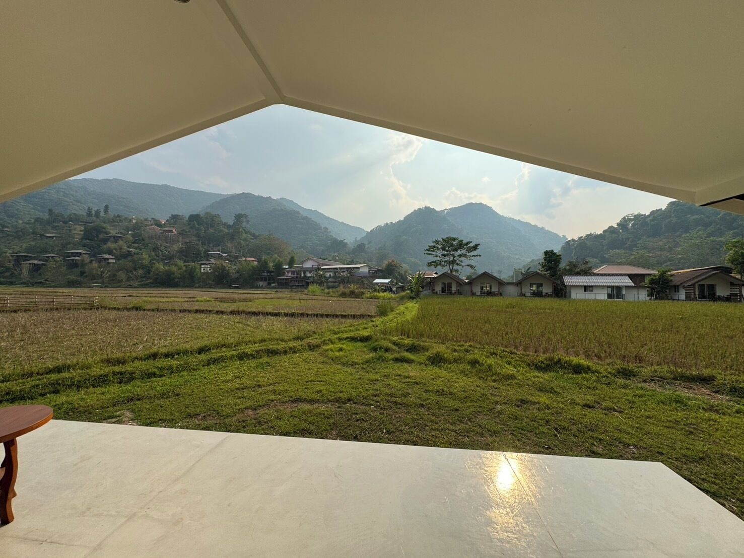 A view from a covered outdoor area with a concrete floor, looking out over a rural landscape with fields and scattered houses.