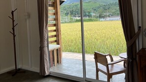 A room with a large sliding glass door leading to a balcony with a view of a rice field and mountains. - Sapan Dee View (Bo Kluea)
