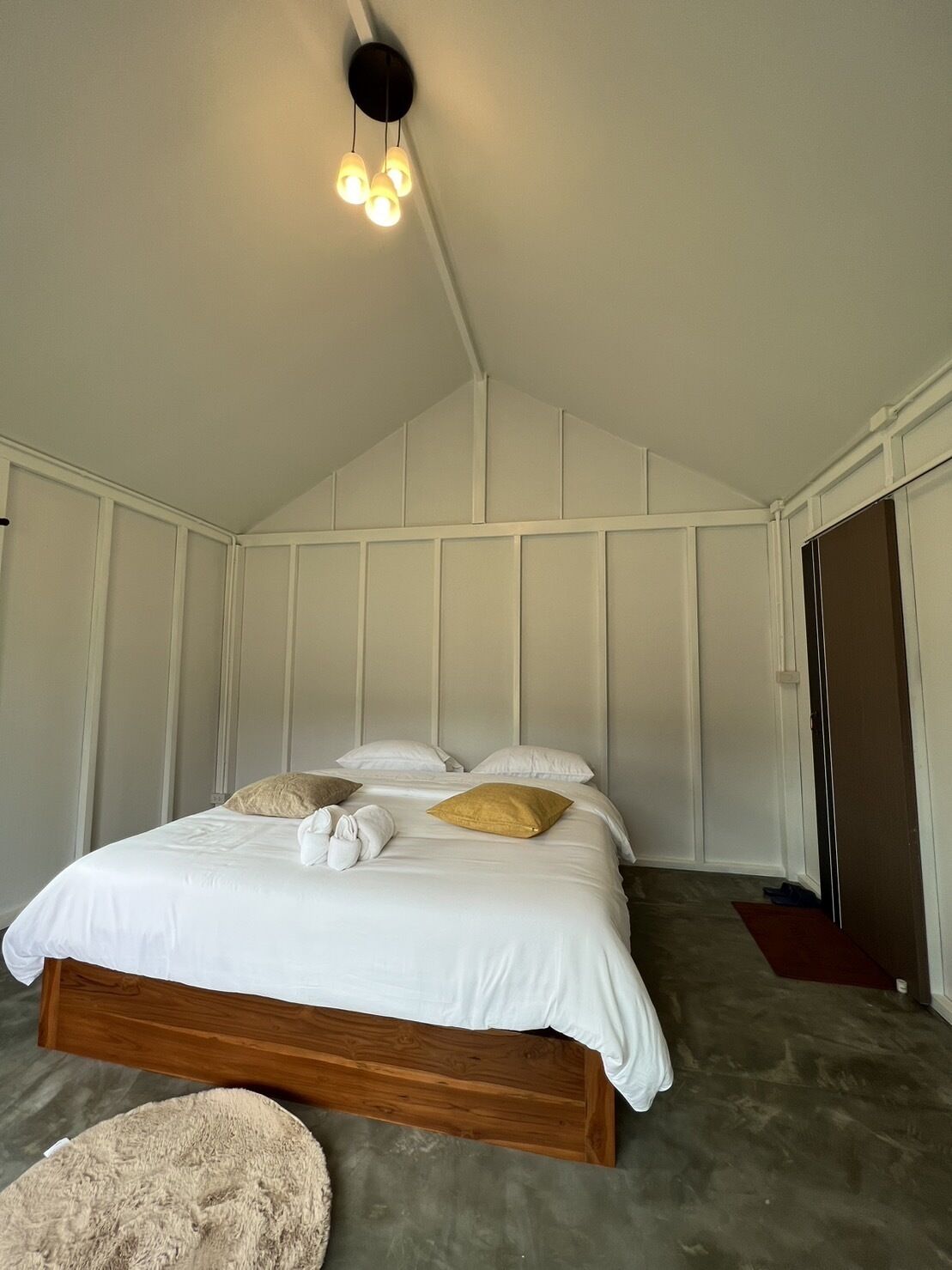 Un dormitorio con cama de madera, ropa de cama blanca y una lámpara en el techo.