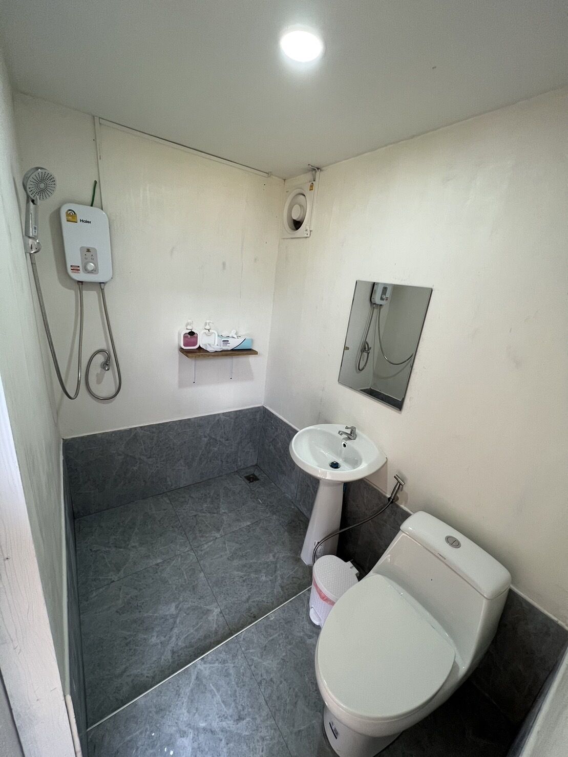 A bathroom with a shower, sink, toilet, and a small shelf with toiletries.