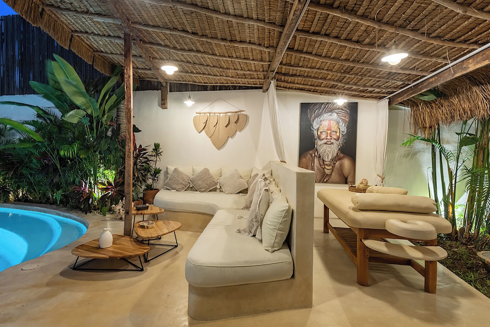 Un salon moderne avec une piscine, un canapé, une table de massage et un plafond au décor de chaume.