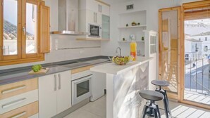 A modern kitchen with wooden cabinets, a built-in oven, a microwave, and a large island with stools. - Pont del Moncau by Interhome (Altea)