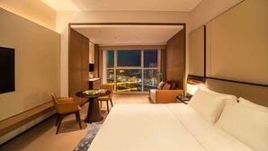 A modern hotel room with a large bed, a seating area with a table, and a view of a cityscape at night. - Wyndham Grand Plaza Royale Yujia Anhua (Yiyang)