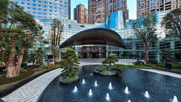 A modern building with a glass facade, a central fountain, and surrounding greenery. - Wyndham Grand Plaza Royale Yujia Anhua (Yiyang)