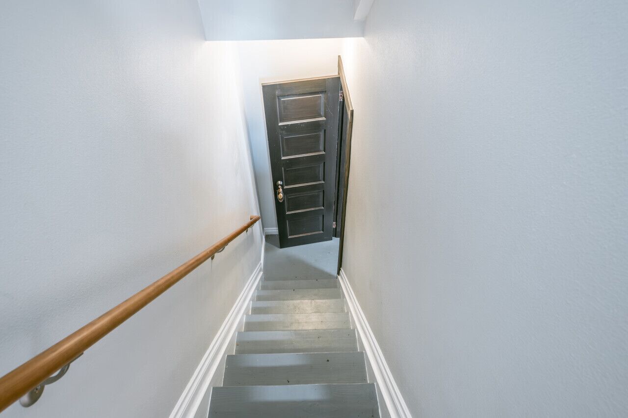 A staircase with a wooden handrail leading to a dark door at the top.