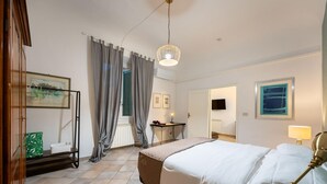 Ett hotellrum med en säng, ett skrivbord, en stol, en hängande lampa och ett fönster med gardiner.