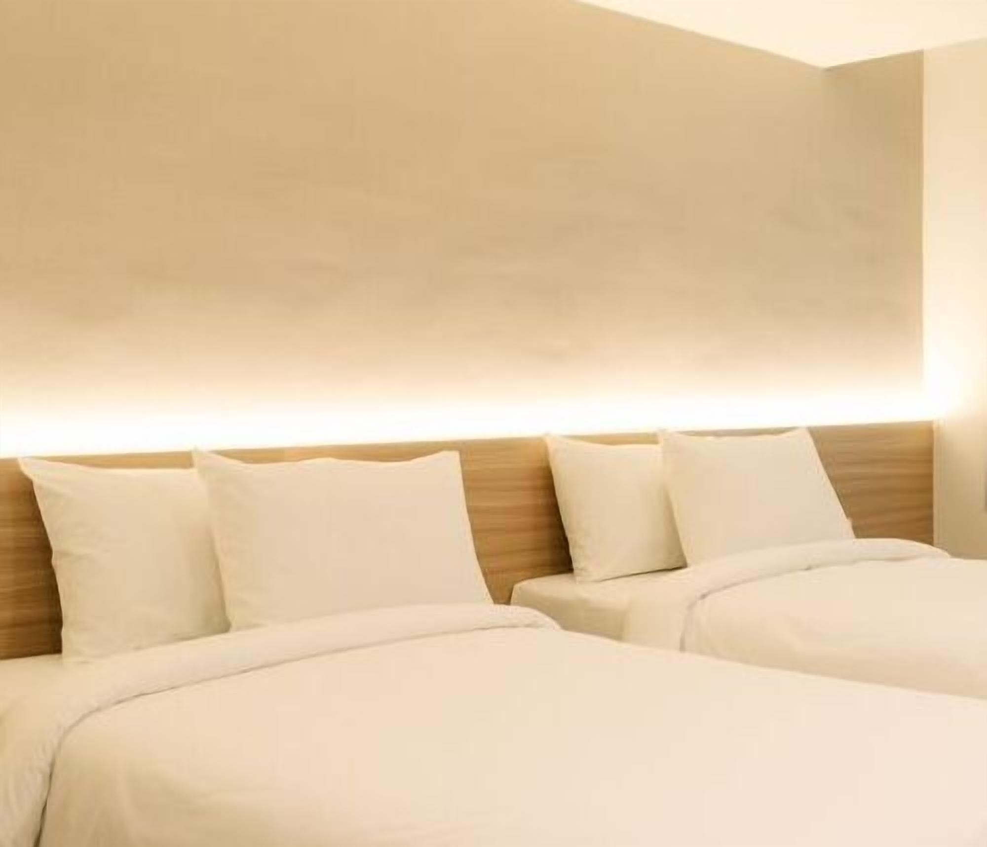 Habitación de hotel con dos camas, cabecero de madera y lámpara fijada a la pared.