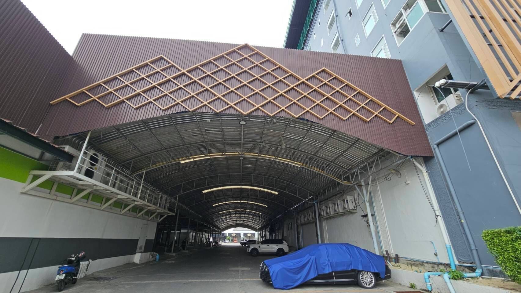Un área de estacionamiento techada con techo metálico y un automóvil cubierto con un lona azul.