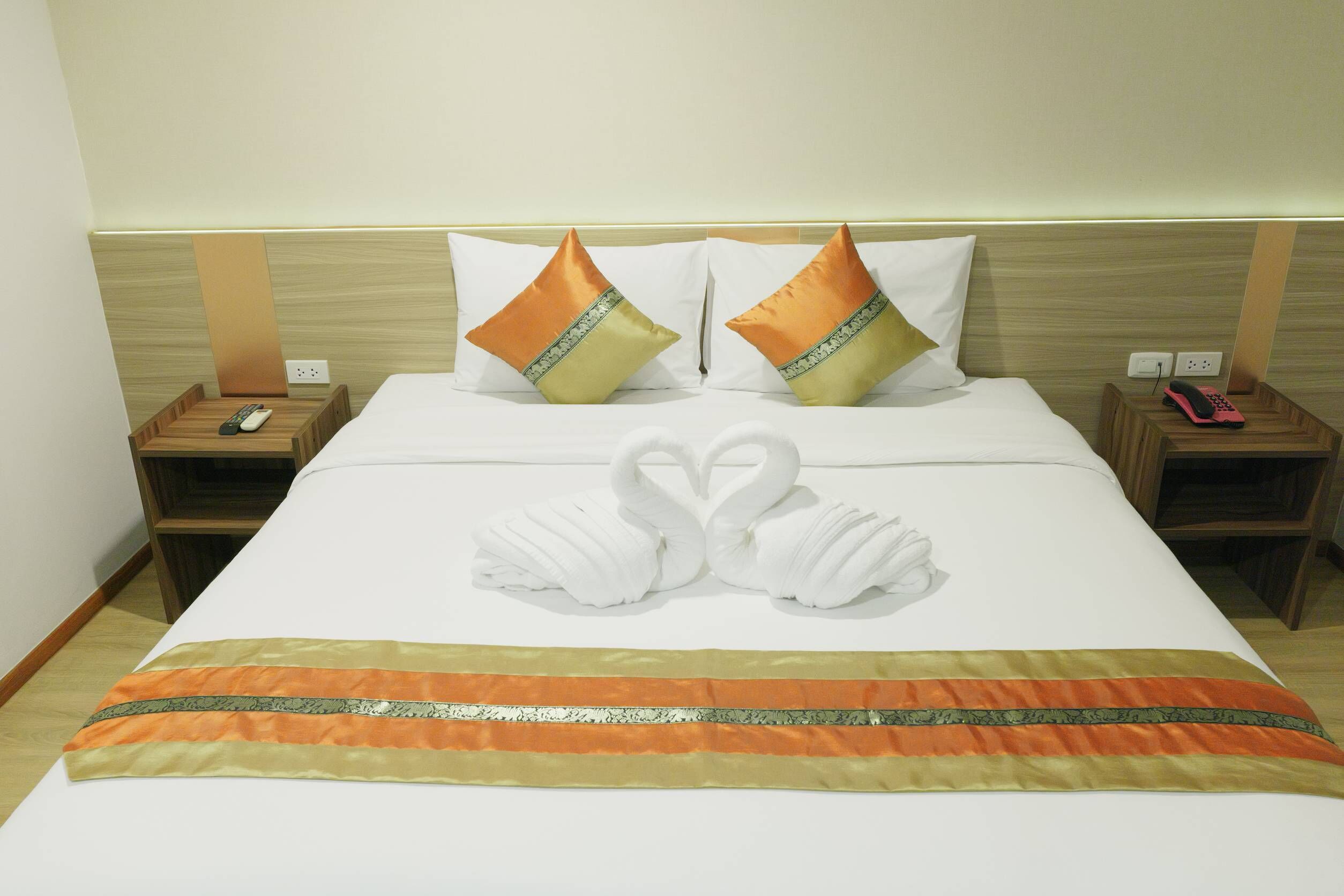 Una habitación de hotel con una cama bien hecha, dos almohadas, un par de toallas con forma de cisne y un teléfono en la mesita de noche.