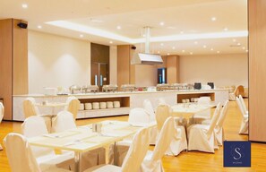 Un salón de banquetes con varias mesas y sillas, un mostrador de buffet y una cocina moderna.