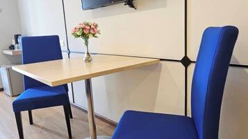 A modern room with a wooden table, two blue chairs, a flat-screen TV mounted on the wall, and a vase with pink flowers on the table.