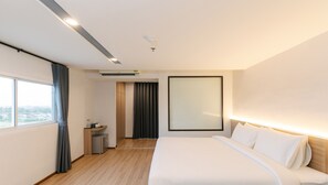 Une chambre d’hôtel avec un lit, un bureau, une chaise, une petite table, un miroir et une fenêtre.