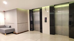 Een moderne liftruimte met een grijze bank, een bedieningspaneel aan de muur en twee liften.