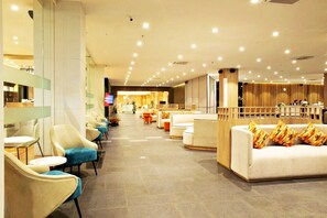 Un hall de hotel con zonas de estar, mostrador de recepción y una pantalla de televisión.