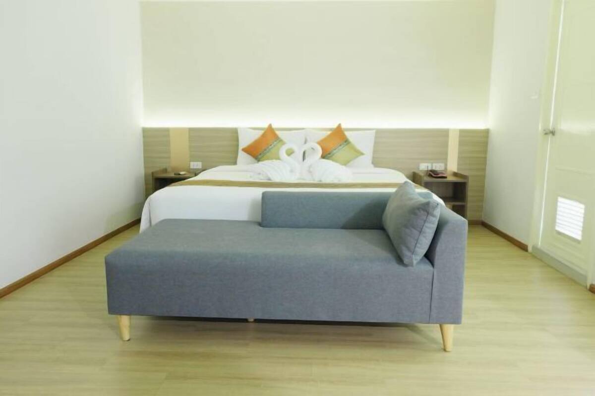 Een moderne hotelkamer met een bed, een grijze bank, een nachtkastje en een bijzettafeltje.