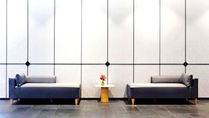 Una habitación moderna con dos sofás enfrentados, una pequeña mesa redonda con un florero y una pared grande con un diseño geométrico.
