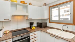 A modern kitchen with white cabinets, a granite countertop, a built-in oven, a microwave, and a window with a view of buildings.