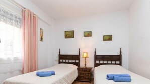 A hotel room with two single beds, a nightstand with a lamp, and a window with curtains.