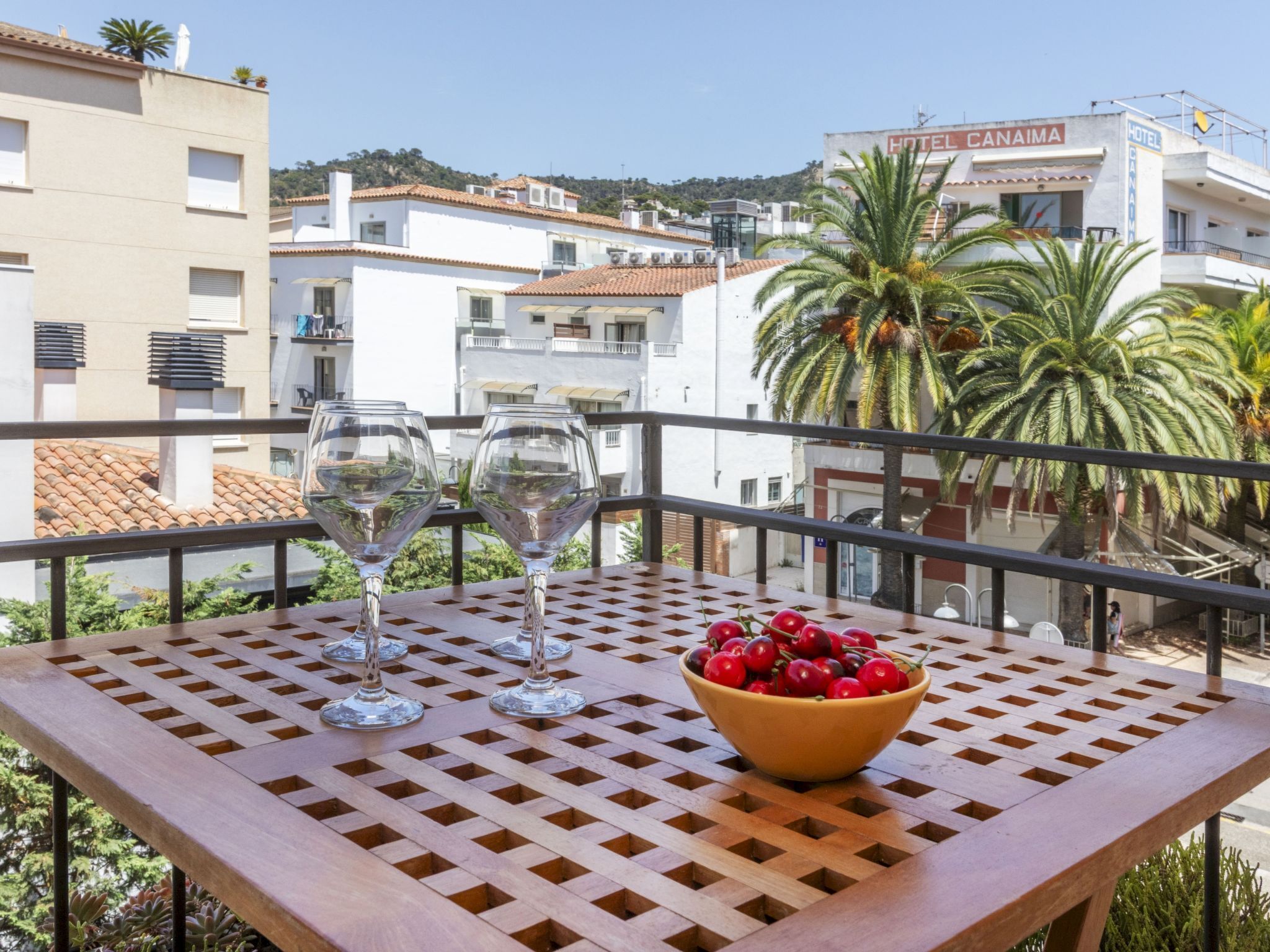 Un balcon avec une table, deux verres à vin et un bol de cerises.