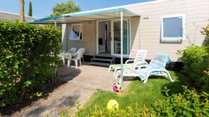 Une maison mobile dotée d’un patio couvert, d’un espace salon extérieur et d’un petit jardin.