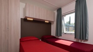 Une chambre avec deux lits simples, une armoire, une fenêtre avec des rideaux et une tête de lit dotée d’un éclairage intégré.