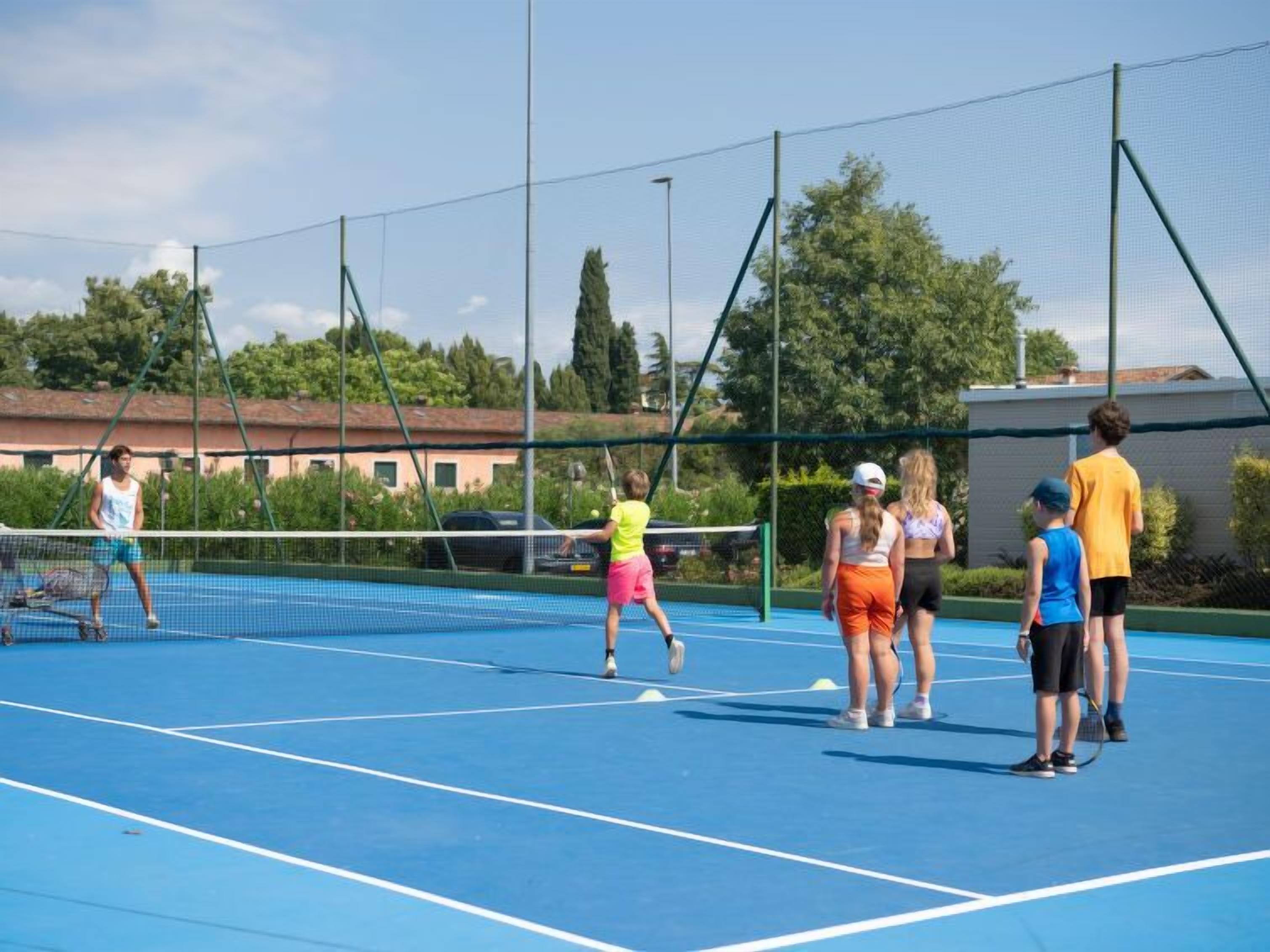 Ulkotenniskenttä, jossa on verkko, ja jonka ympärillä on aita ja puita.