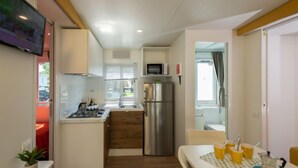 A compact kitchen with a stove, sink, and refrigerator, a dining table with yellow cups, and a TV mounted on the wall. - Garda Family Plus by Interhome (Desenzano)