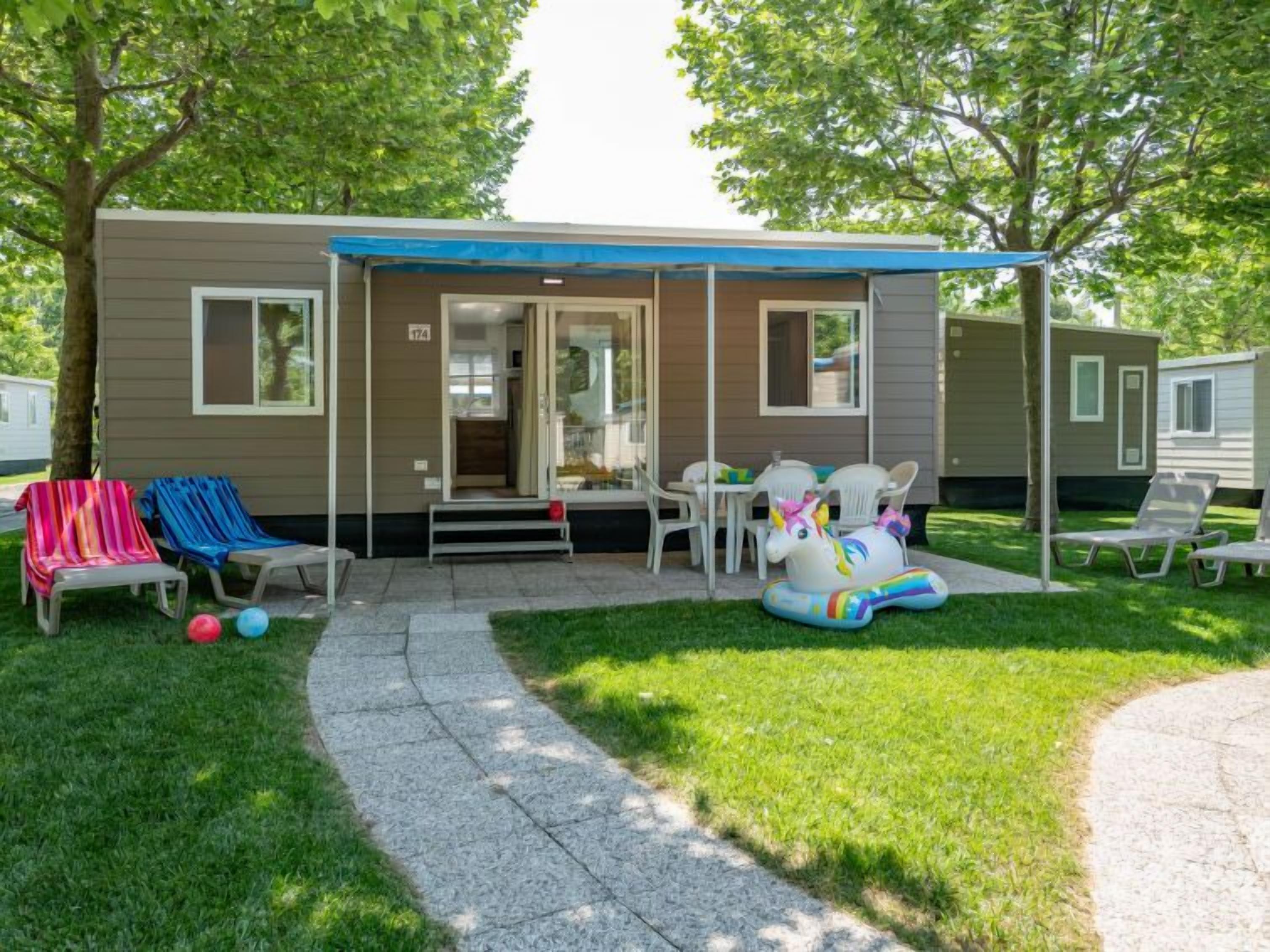 A mobile home with a covered patio, outdoor seating, and a lawn.