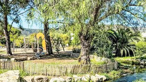 A park with a small stream, trees, and a wooden fence. - L'Alicastre by Interhome (Le Lavandou)