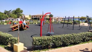 An outdoor playground with swings and a seesaw, surrounded by neatly trimmed hedges and a clear sky. - Le Bijou by Interhome (Cannigione)