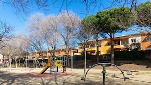A playground with swings, slides, and climbing structures, surrounded by trees and residential buildings. - La Victoria by Interhome (Palafrugell)
