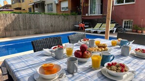 A breakfast setup by a poolside with a checkered tablecloth, plates of fruit, cereal, and beverages. - La Victoria by Interhome (Palafrugell)