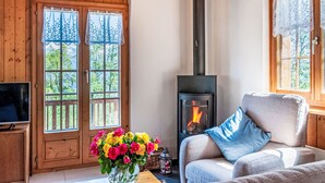 A cozy room with wooden walls, a fireplace, a sofa with a blue pillow, and a TV on a wooden cabinet.