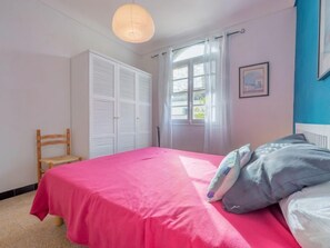 A bedroom with a bed, a chair, a wardrobe, and a window with curtains.