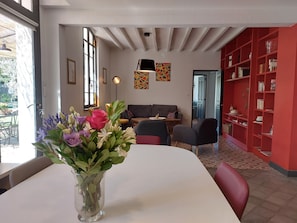 A modern living room with a white table, a vase of flowers, a grey sofa, and a red bookshelf.