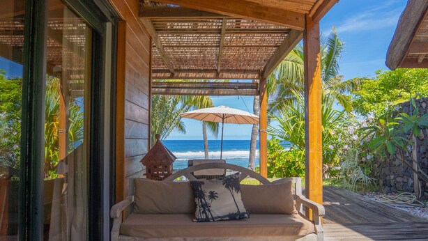 A covered outdoor seating area with a wooden ceiling, a cushioned bench, and a table. - ST GILLES, CHARMING HOUSE, seaside, Coral villa, lagoon, 4 **** (Saint Paul)