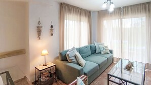 A living room with a sofa, a glass coffee table, a lamp, and a small side table.