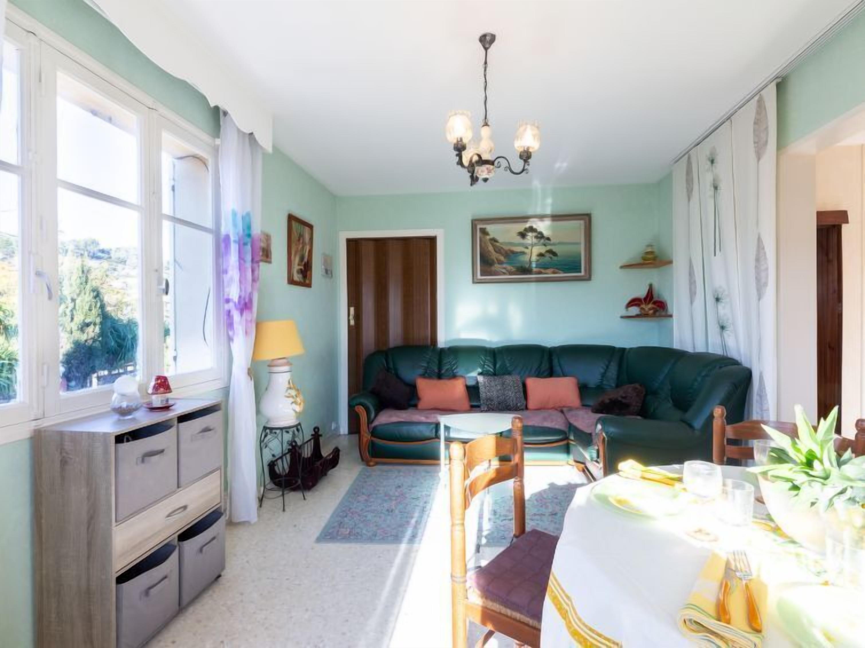 Un salon chaleureux avec un canapé vert, une table à manger dressée pour deux personnes et un lustre.