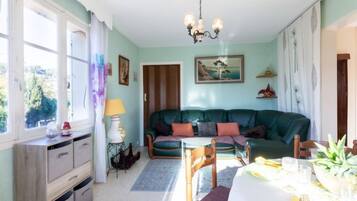 Un salon chaleureux avec un canapé vert, une table à manger dressée pour deux personnes et un lustre.