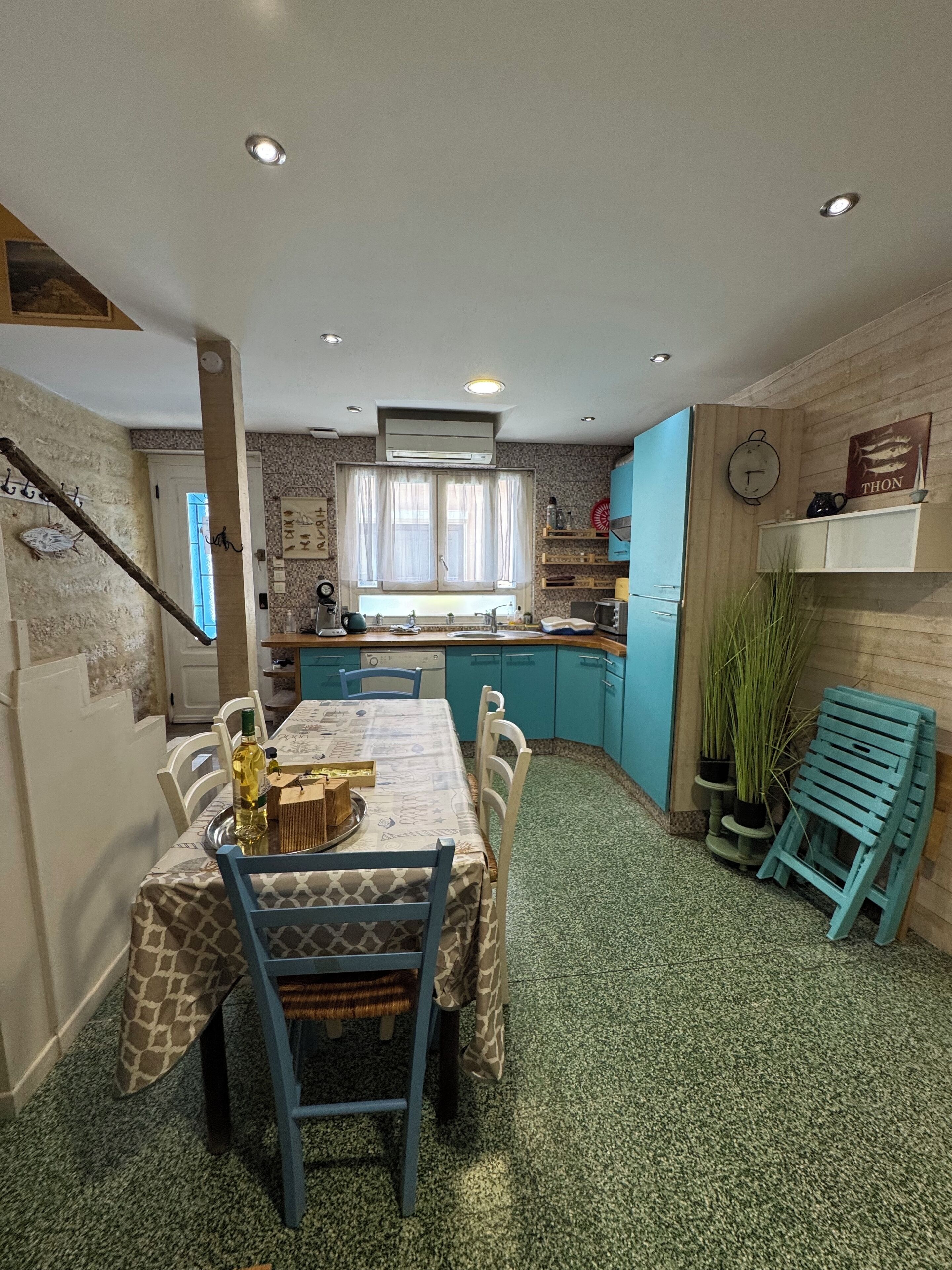 A kitchen with a dining area, featuring a table with chairs, a window with curtains, and a clock on the wall.