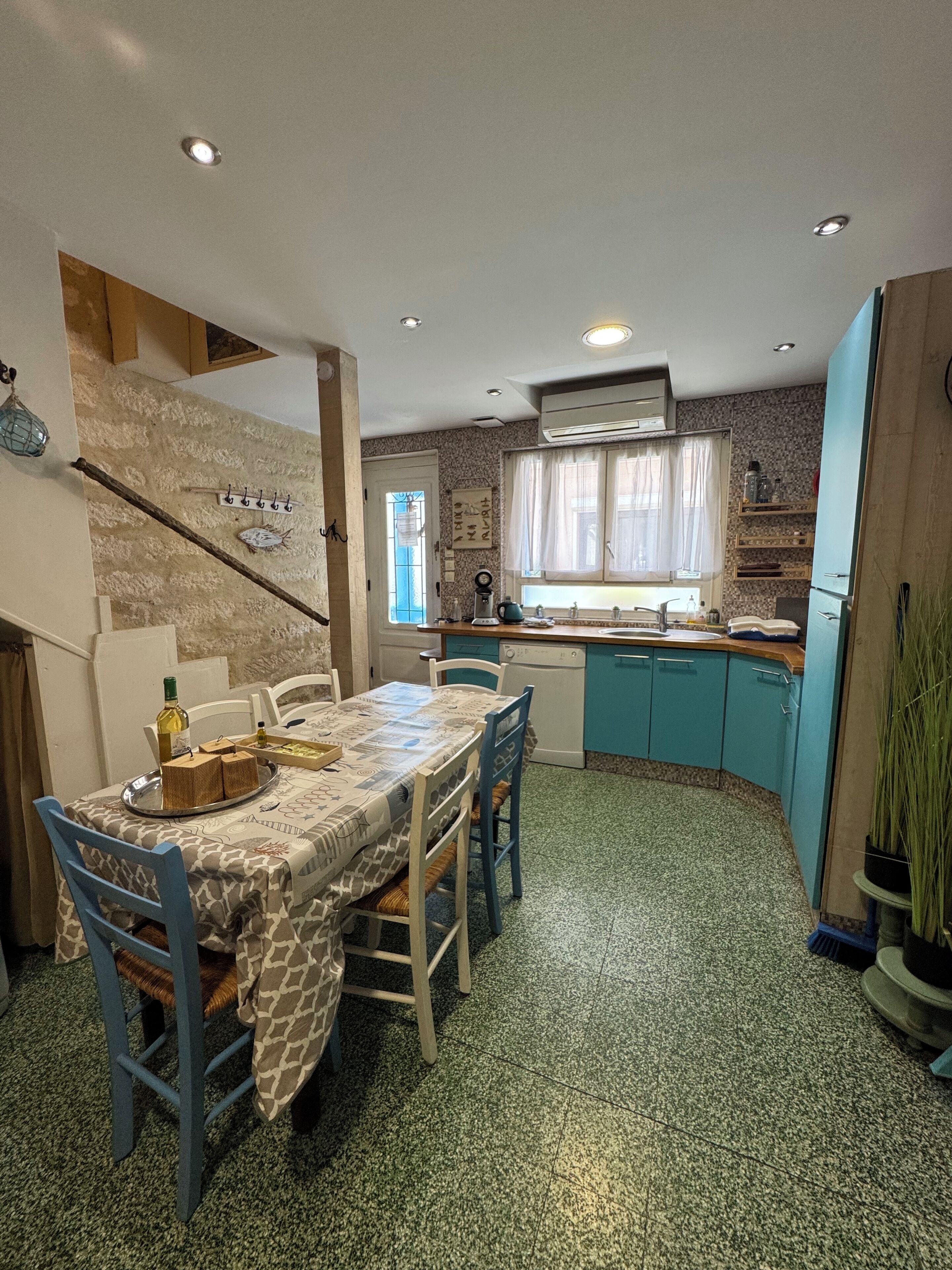A dining area with a table set for four, a kitchen with teal cabinets, and a staircase with a decorative fish wall.