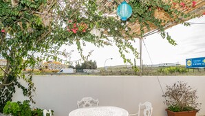 Un espacio al aire libre cubierto con una mesa redonda y sillas, rodeado de plantas en macetas y flores colgantes.